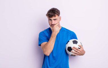 young handsome man with mouth and eyes wide open and hand on chin. soccer concept