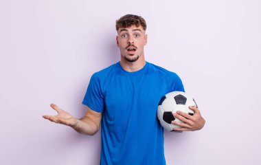 young handsome man feeling extremely shocked and surprised. soccer concept
