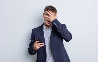 young handsome man looking shocked, scared or terrified, covering face with hand. business concept