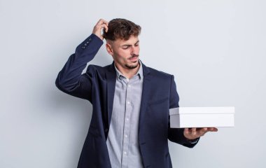 Kafası karışmış, kafası karışmış, kaşınan genç, yakışıklı bir adam. beyaz kutu paketi