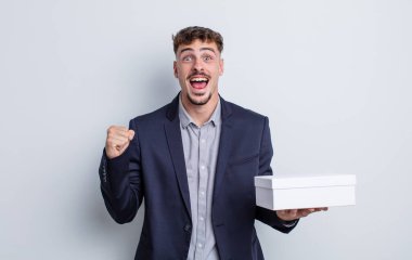 Genç yakışıklı adam şok olmuş hissediyor, gülüyor ve başarıyı kutluyor. beyaz kutu paketi