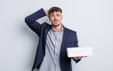 Genç ve yakışıklı bir adam stresli, endişeli ya da korkmuş hissediyor. Elleri başının üstünde. beyaz kutu paketi