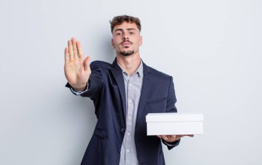 Genç ve yakışıklı adam ciddi görünüyor. Avuç içi gösteriyor. Durdurma hareketi yapıyor. beyaz kutu paketi