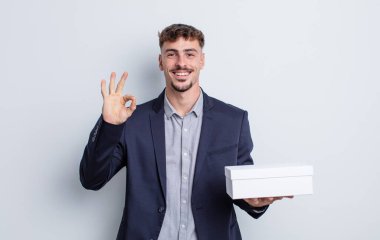 Genç yakışıklı adam kendini mutlu hissediyor, iyi bir jestle onaylıyor. beyaz kutu paketi