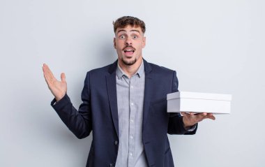 Genç yakışıklı adam kendini mutlu hissediyor ve inanılmaz bir şeye hayret ediyor. beyaz kutu paketi