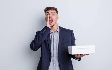 Genç yakışıklı adam mutlu hissediyor, elleri ağzının kenarında bağırıyor. beyaz kutu paketi