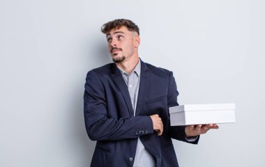 Genç yakışıklı adam omuz silkiyor, kafası karışık ve kararsız. beyaz kutu paketi