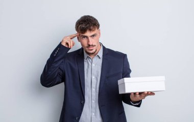 Genç yakışıklı adam kafası karışık ve şaşkın hissediyor, deli olduğunu gösteriyor. beyaz kutu paketi