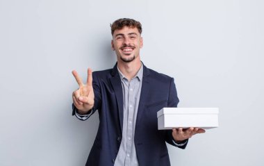 Genç yakışıklı adam gülümsüyor ve arkadaş canlısı görünüyor, iki numarayı gösteriyor. beyaz kutu paketi