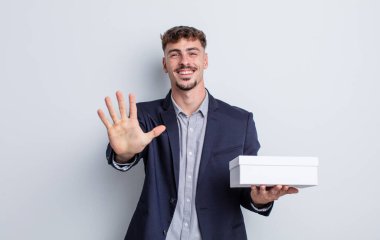 Genç yakışıklı adam gülümsüyor ve arkadaş canlısı görünüyor, beş numarayı gösteriyor. beyaz kutu paketi