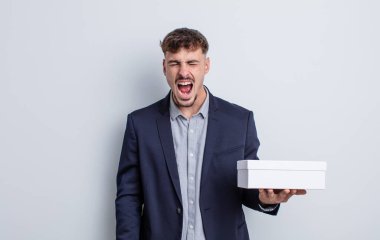 Genç yakışıklı adam agresif bir şekilde bağırıyor, çok kızgın görünüyor. beyaz kutu paketi