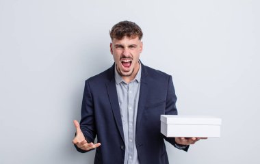 Genç ve yakışıklı bir adam sinirli, sinirli ve sinirli görünüyor. beyaz kutu paketi
