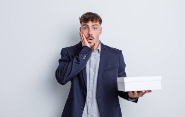 Genç ve yakışıklı bir adam şok olmuş ve korkmuş hissediyor. beyaz kutu paketi