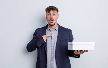 Şok olmuş ve ağzı açık, kendini işaret eden genç ve yakışıklı bir adam. beyaz kutu paketi