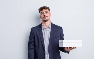 Kafası karışmış ve kafası karışmış genç yakışıklı bir adam. beyaz kutu paketi