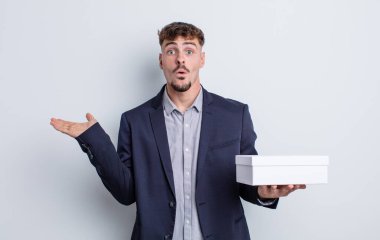 Genç, yakışıklı adam şaşırmış ve şok olmuş görünüyor. Çenesi düşmüş, elinde bir nesne var. beyaz kutu paketi