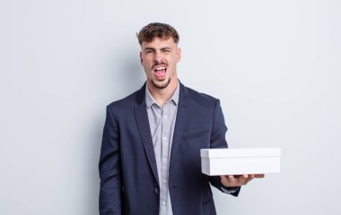 Genç ve yakışıklı bir adam tiksinmiş ve sinirlenmiş hissediyor ve dilini dışarı çıkarıyor. beyaz kutu paketi