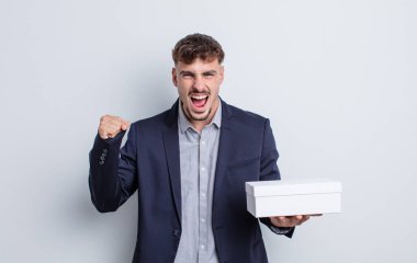 Genç yakışıklı adam sinirli bir ifadeyle agresif bir şekilde bağırıyor. beyaz kutu paketi