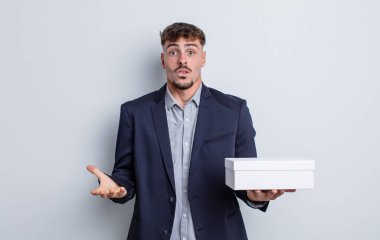 Genç ve yakışıklı bir adam şok olmuş ve şaşırmış hissediyor. beyaz kutu paketi