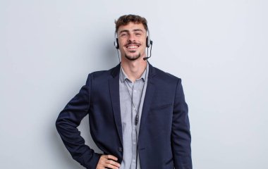 Genç yakışıklı adam mutlu bir şekilde gülümsüyor, eli kalçasında ve kendinden emin. tele pazarlamacı kavramı