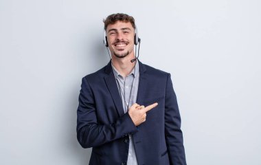 Genç yakışıklı adam neşeyle gülümsüyor, mutlu hissediyor ve bir tarafı işaret ediyor. tele pazarlamacı kavramı