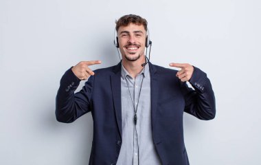 Genç ve yakışıklı bir adam kendi gülüşünü işaret ederek kendine güvenerek gülümsüyor. tele pazarlamacı kavramı