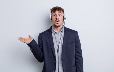 Genç, yakışıklı adam şaşırmış ve şok olmuş görünüyor. Çenesi düşmüş, elinde bir nesne var. tele pazarlamacı kavramı