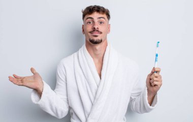 Genç yakışıklı adam şaşkın, şaşkın ve şüpheci hissediyor. diş fırçası kavramı
