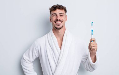 Genç yakışıklı adam mutlu bir şekilde gülümsüyor, eli kalçasında ve kendinden emin. diş fırçası kavramı