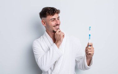 Genç ve yakışıklı bir adam mutlu ve kendinden emin bir ifadeyle gülümsüyor, elleri çenesinde. diş fırçası kavramı