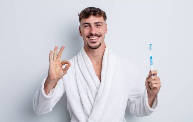 Genç yakışıklı adam kendini mutlu hissediyor, iyi bir jestle onaylıyor. diş fırçası kavramı