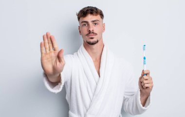 Genç ve yakışıklı adam ciddi görünüyor. Avuç içi gösteriyor. Durdurma hareketi yapıyor. diş fırçası kavramı