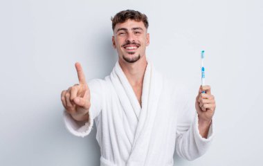 Genç yakışıklı adam gülümsüyor ve arkadaş canlısı görünüyor, bir numarayı gösteriyor. diş fırçası kavramı