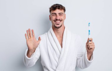 Genç yakışıklı adam mutlu bir şekilde gülümsüyor, el sallıyor, sizi selamlıyor ve selamlıyor. diş fırçası kavramı