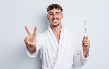 Genç yakışıklı adam gülümsüyor ve arkadaş canlısı görünüyor, iki numarayı gösteriyor. diş fırçası kavramı