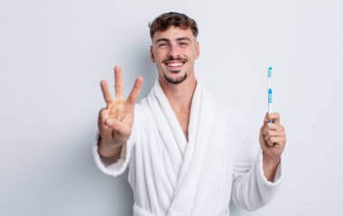 Genç yakışıklı adam gülümsüyor ve arkadaş canlısı görünüyor, üç numarayı gösteriyor. diş fırçası kavramı