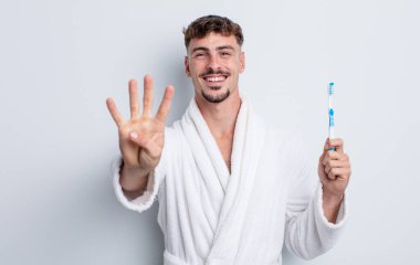 Genç yakışıklı adam gülümsüyor ve arkadaş canlısı görünüyor, dört numarayı gösteriyor. diş fırçası kavramı