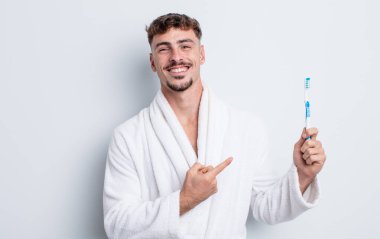 Genç yakışıklı adam neşeyle gülümsüyor, mutlu hissediyor ve bir tarafı işaret ediyor. diş fırçası kavramı