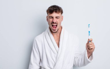 Genç yakışıklı adam agresif bir şekilde bağırıyor, çok kızgın görünüyor. diş fırçası kavramı