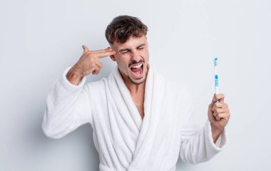 Genç yakışıklı adam mutsuz ve stresli görünüyor, intihar jesti silah işareti yapıyor. diş fırçası kavramı