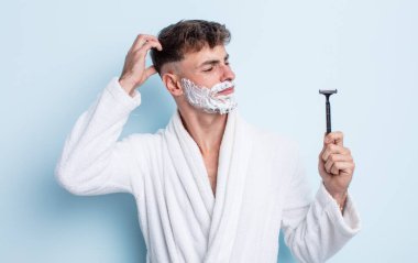 Genç yakışıklı adam mutlu bir şekilde gülümsüyor ve hayal kuruyor ya da şüphe ediyor. traş konsepti