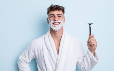 Genç yakışıklı adam mutlu bir şekilde gülümsüyor, eli kalçasında ve kendinden emin. traş konsepti