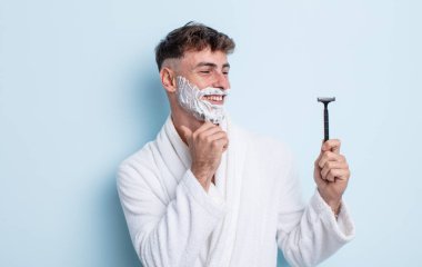 Genç ve yakışıklı bir adam mutlu ve kendinden emin bir ifadeyle gülümsüyor, elleri çenesinde. traş konsepti