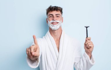 Genç yakışıklı adam gülümsüyor ve arkadaş canlısı görünüyor, bir numarayı gösteriyor. traş konsepti