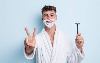 Genç yakışıklı adam gülümsüyor ve arkadaş canlısı görünüyor, iki numarayı gösteriyor. traş konsepti