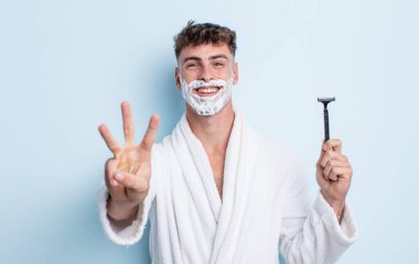 Genç yakışıklı adam gülümsüyor ve arkadaş canlısı görünüyor, üç numarayı gösteriyor. traş konsepti