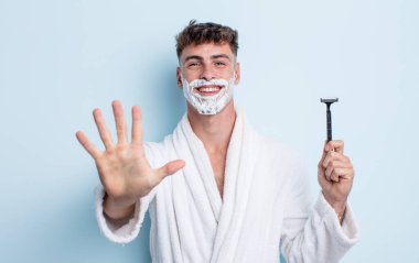 Genç yakışıklı adam gülümsüyor ve arkadaş canlısı görünüyor, beş numarayı gösteriyor. traş konsepti