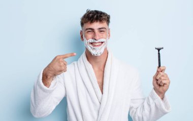 Genç ve yakışıklı bir adam kendi gülüşünü işaret ederek kendine güvenerek gülümsüyor. traş konsepti