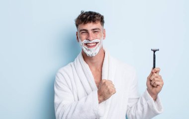 Genç yakışıklı adam kendini mutlu hissediyor ve bir meydan okumayla yüzleşiyor ya da kutluyor. traş konsepti