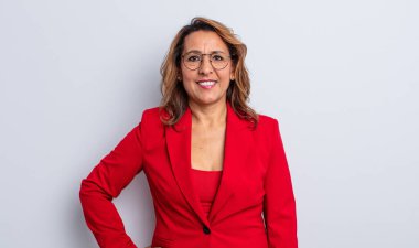 Güzel orta yaşlı bir kadın mutlu bir şekilde gülümsüyor, eli kalçasında ve kendinden emin. İş kadını kavramı